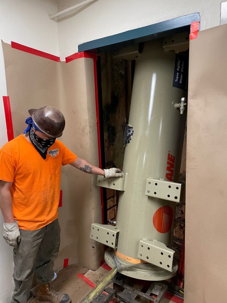 Jobsite photo of a construction worker inside of an elevator shaft, using electric chain hoist rentals from LGH to lift a chiller.