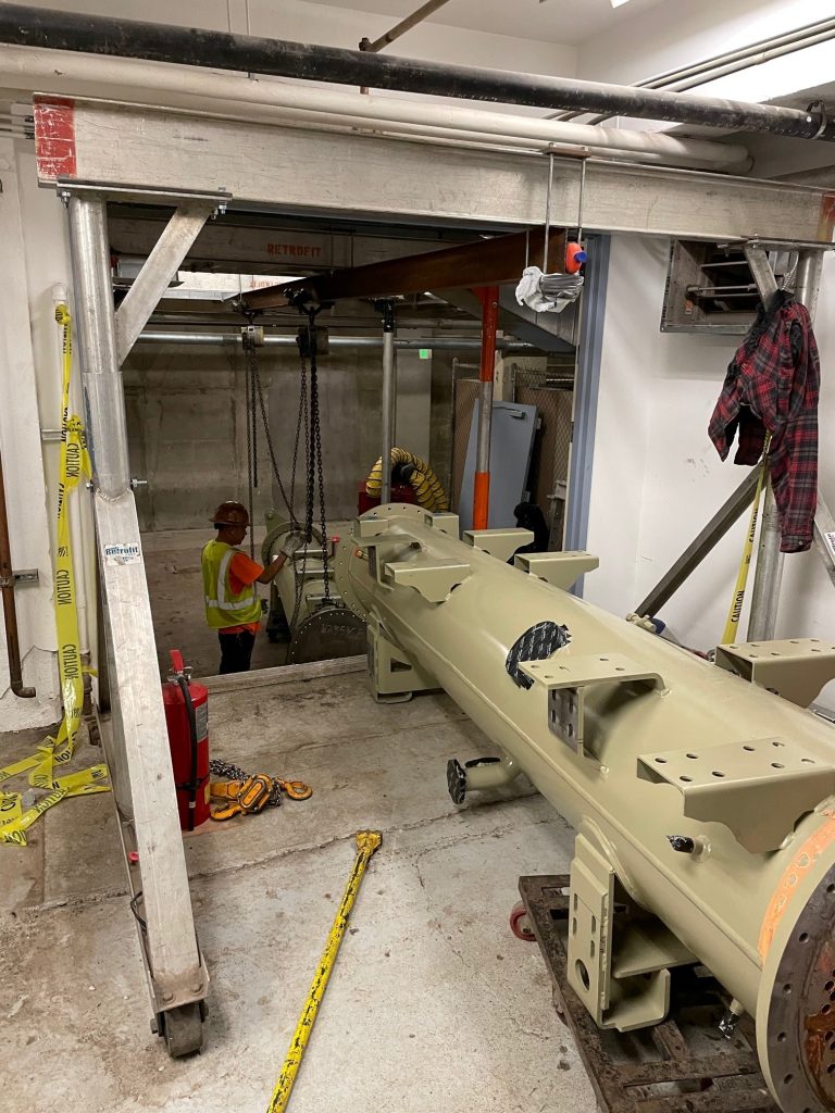 Jobsite photo of a large chiller unit component being lifted inside of an elevator shaft with rigging from LGH.