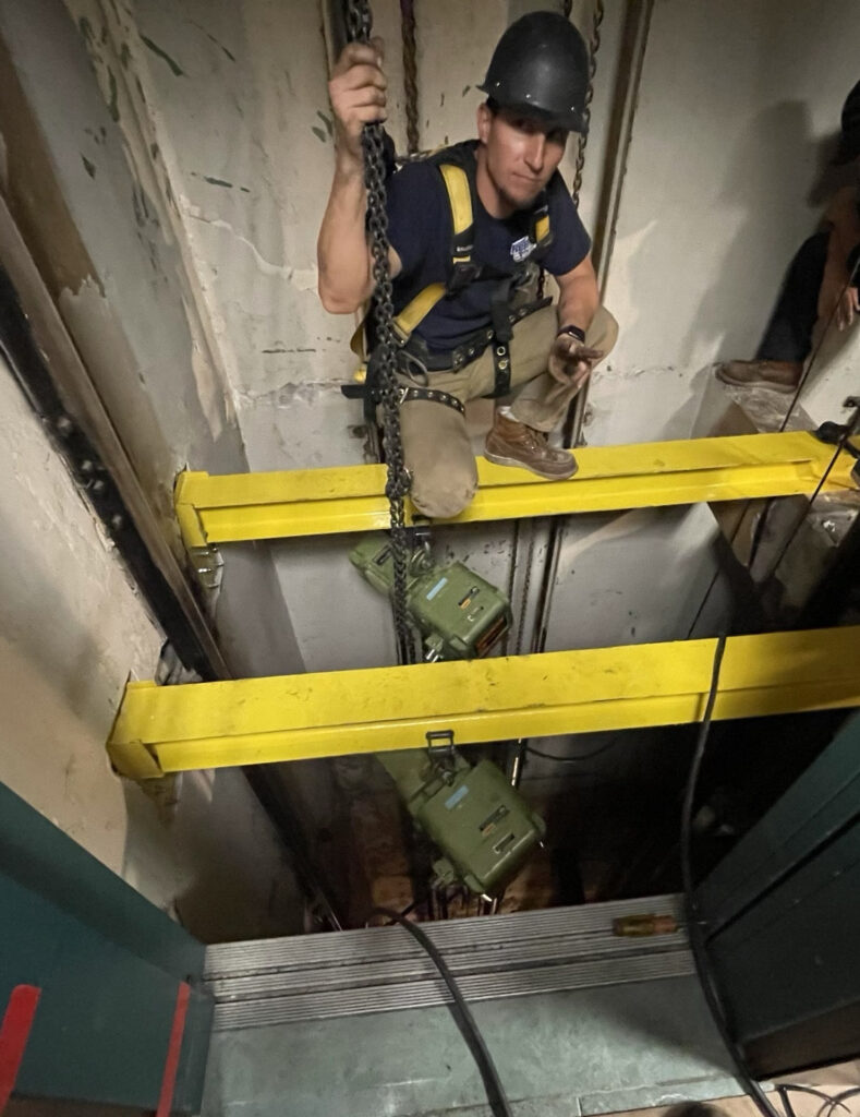 Jobsite photo of a construction worker inside of an elevator shaft, using electric chain hoist rentals from LGH to lift a chiller.