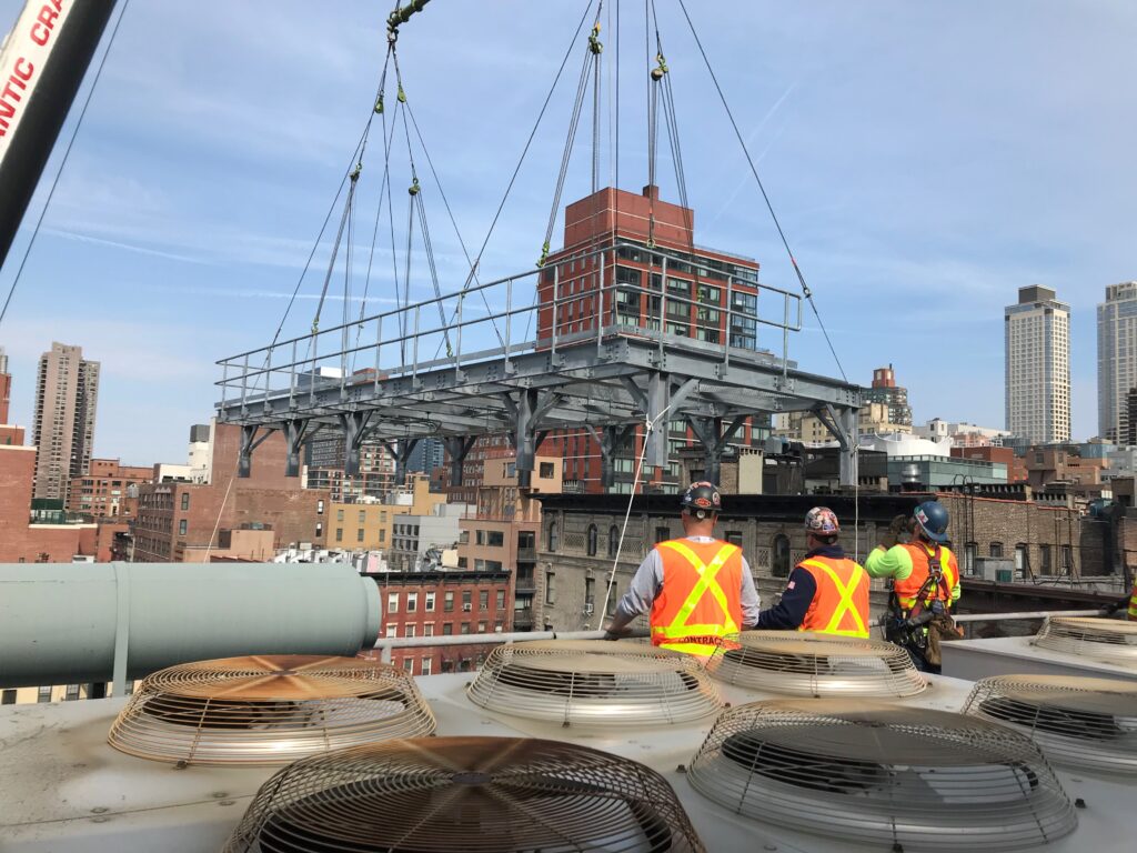 A jobsite photo of a NYC MTA platform lift, demonstrating a below-the-hook rigging configuration with wire rope slings, sheave blocks, and other rigging gear.