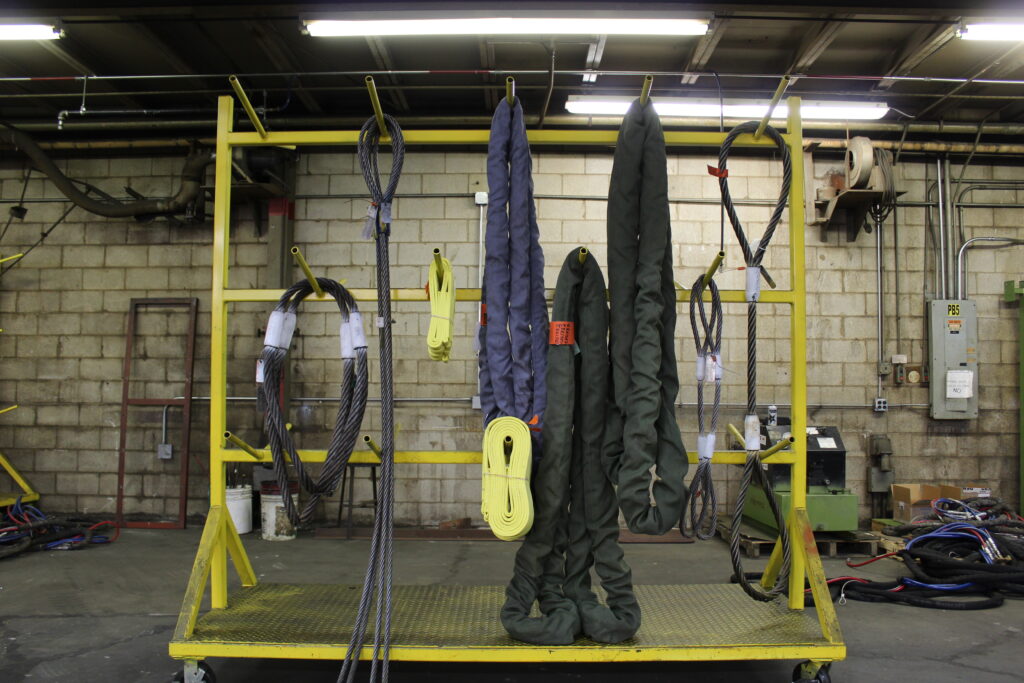 A photo of both wire rope rigging slings and polyester round rigging slings stored on a storage rack in the LGH Rental Center warehouse.
