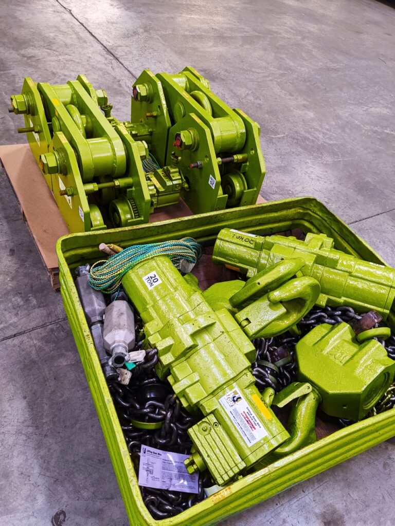 A photo of green LGH air chain hoist rentals, alongside a couple of beam trolley rentals, in a shipping container with chain.