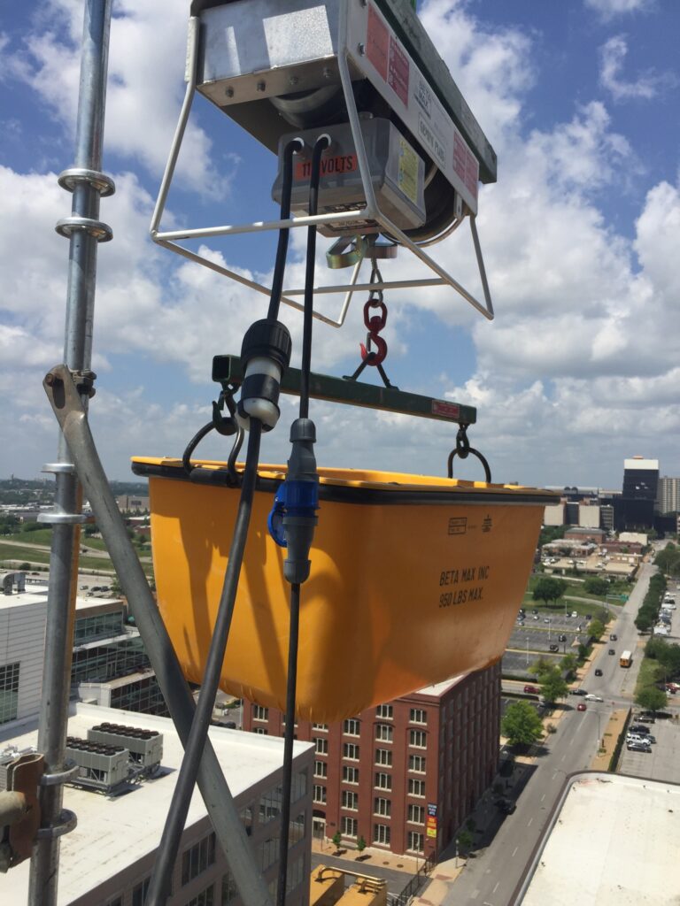 A Beta Max electric cable hoist rental from LGH on a jobsite, with a bucket attached to the wire rope for lifting supplies.