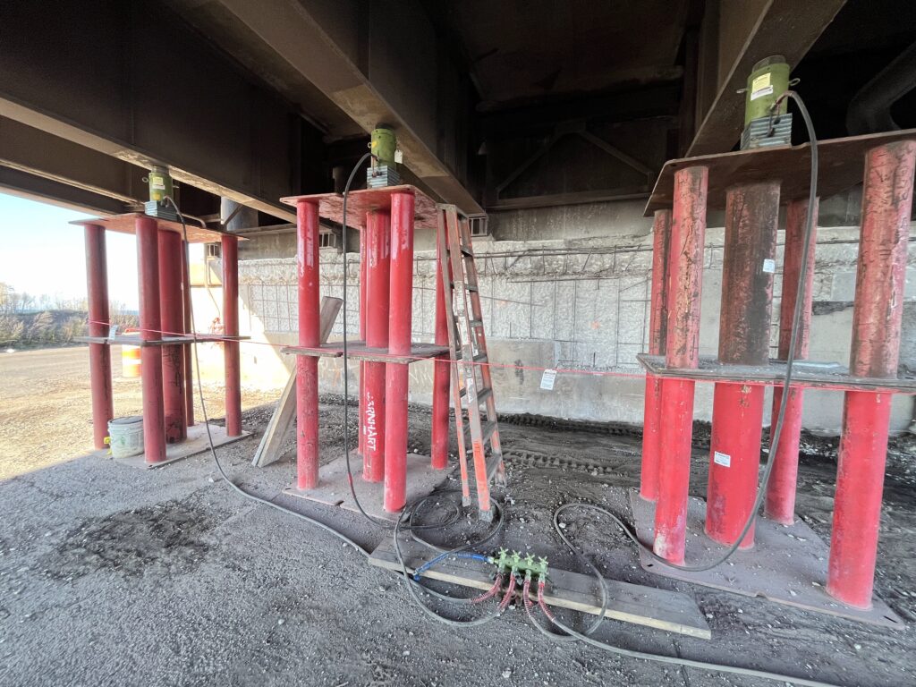 Jobsite photo of hydraulic ram jacks under a bridge with hydraulic manifold.