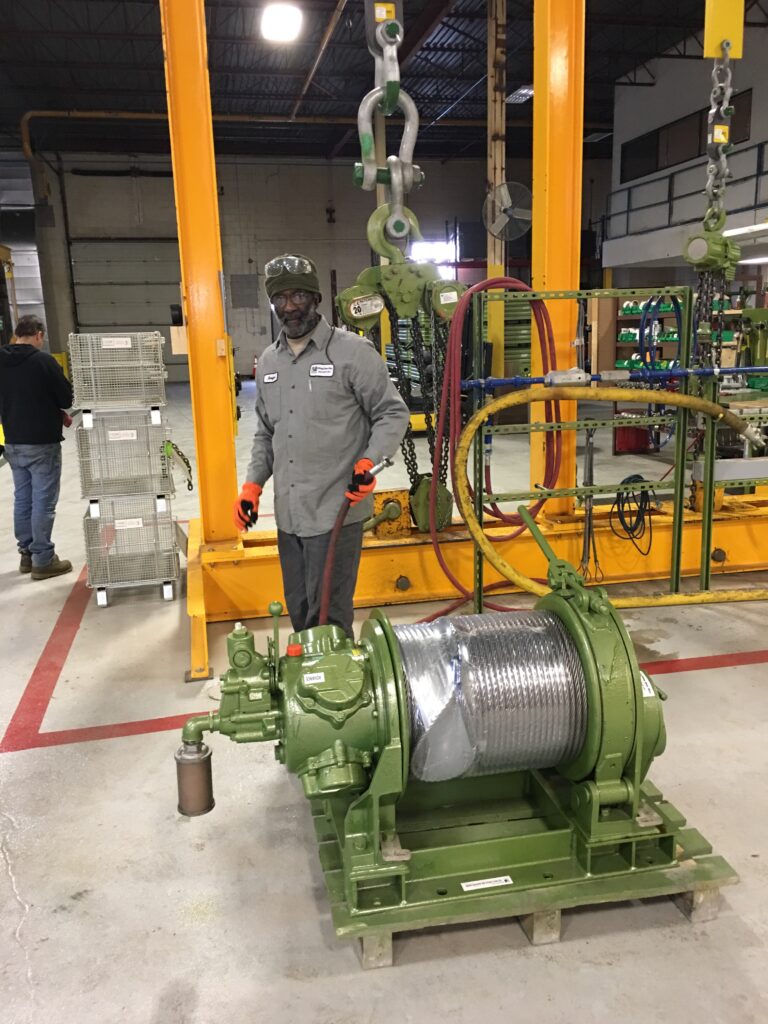 A photo inside the LGH Rental Center warehouse of an air winch with a worker and testing stand in the background.