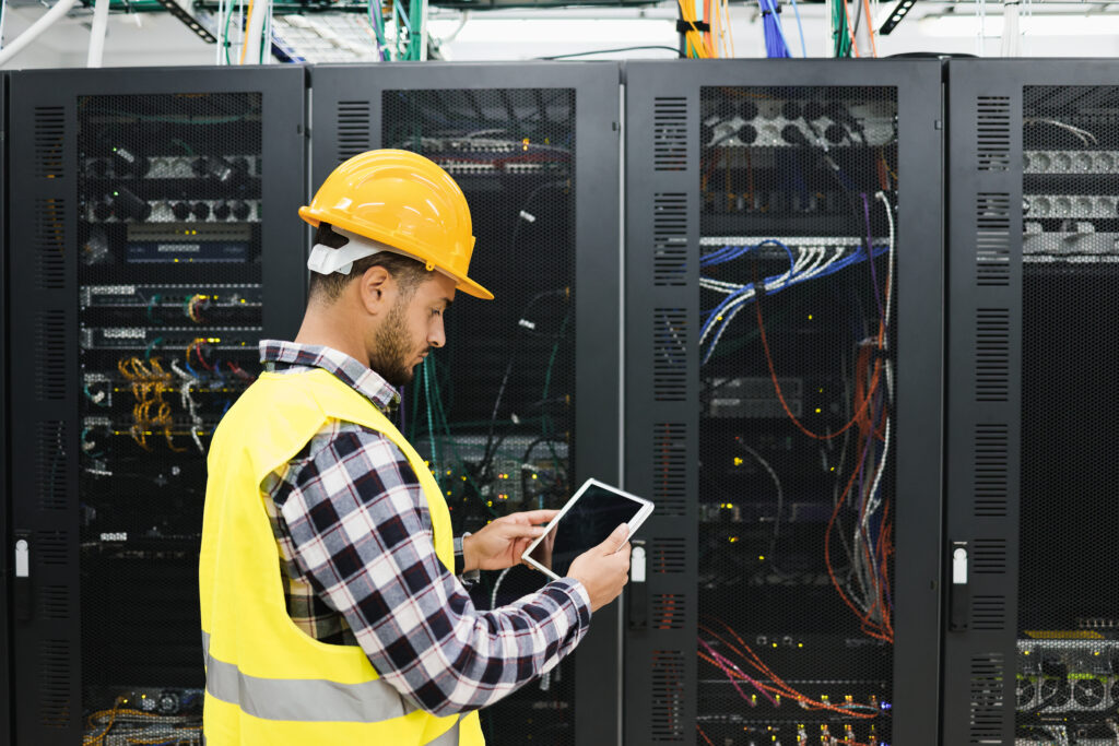 Young technician man working with tablet inside big data center room - Focus on right hand holding tablet