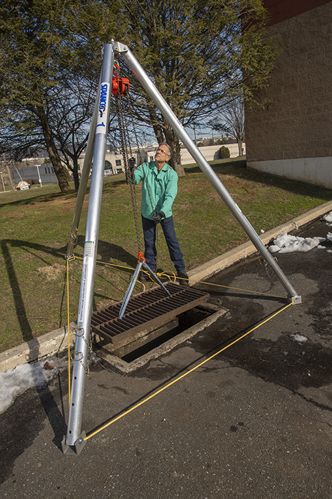 A man pulling a chain hoist from an aluminum tripod hoist crane rental from LGH.
