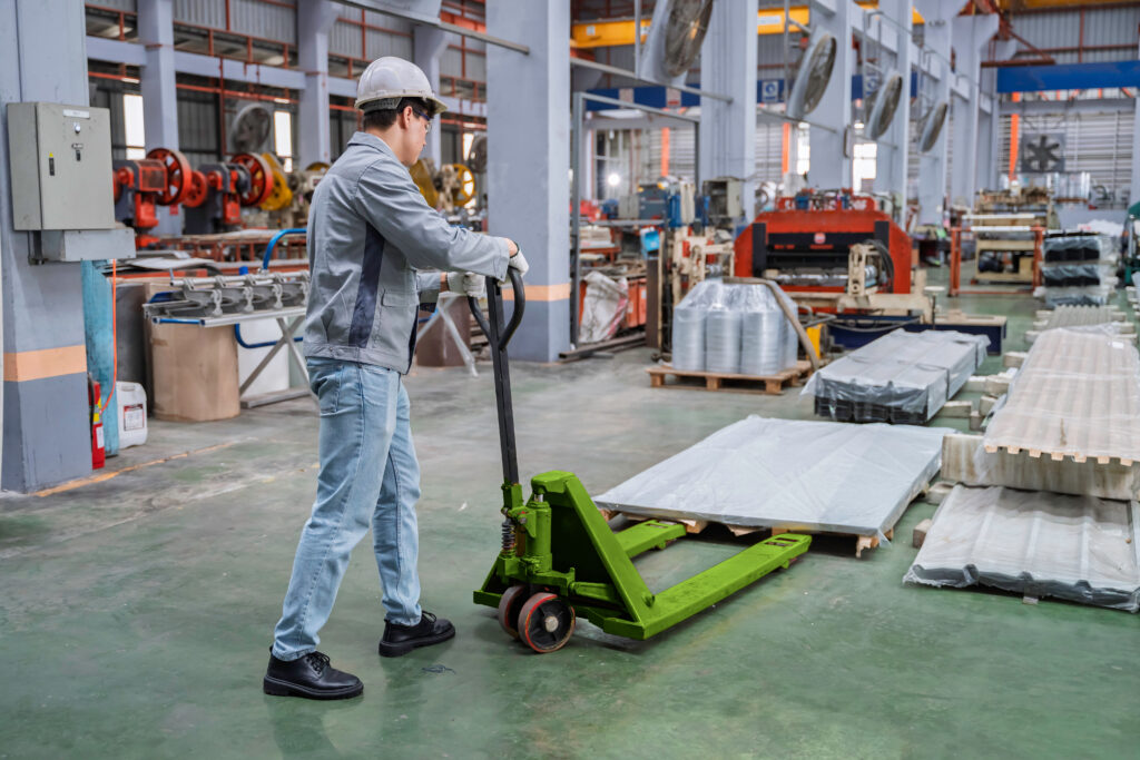 A stock photo example of an industrial construction worker using a green manual pallet jack to move a heavy load.