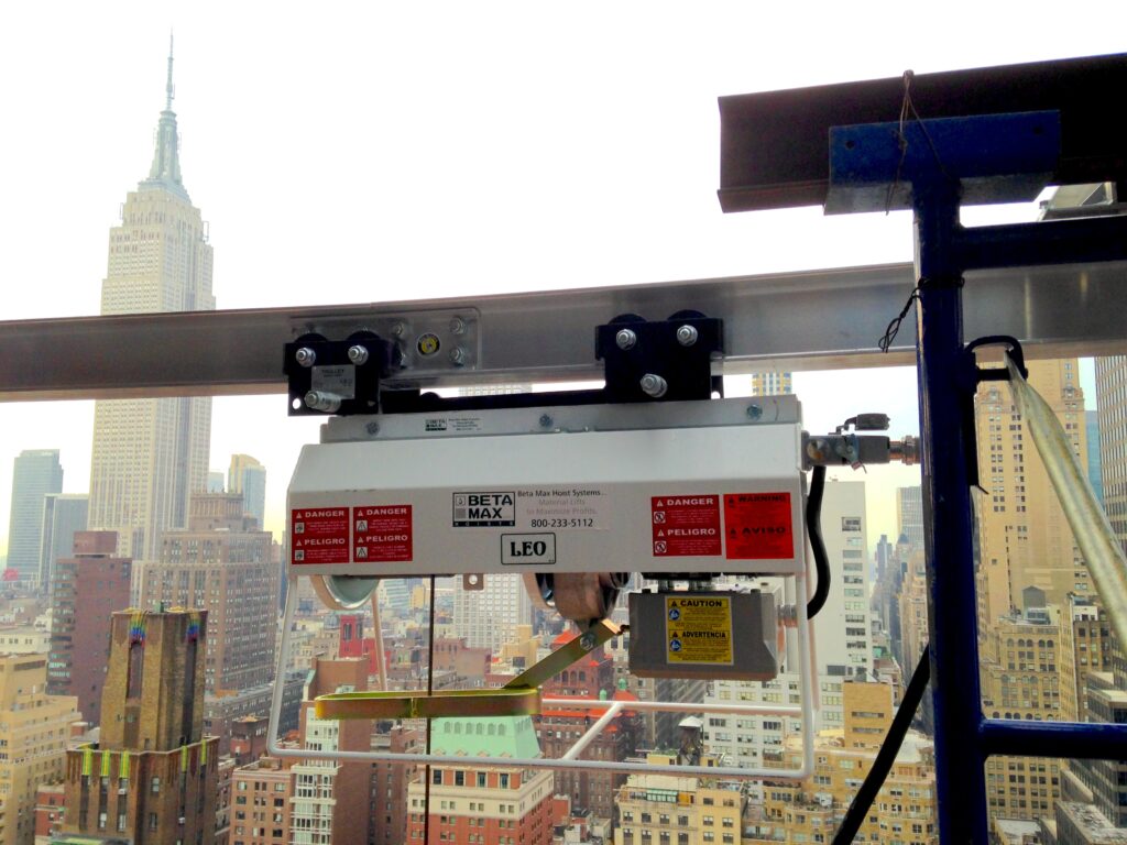 Jobsite photo of the Beta Max Leo Hoist attached to a track system, with the Empire State Building in the background.