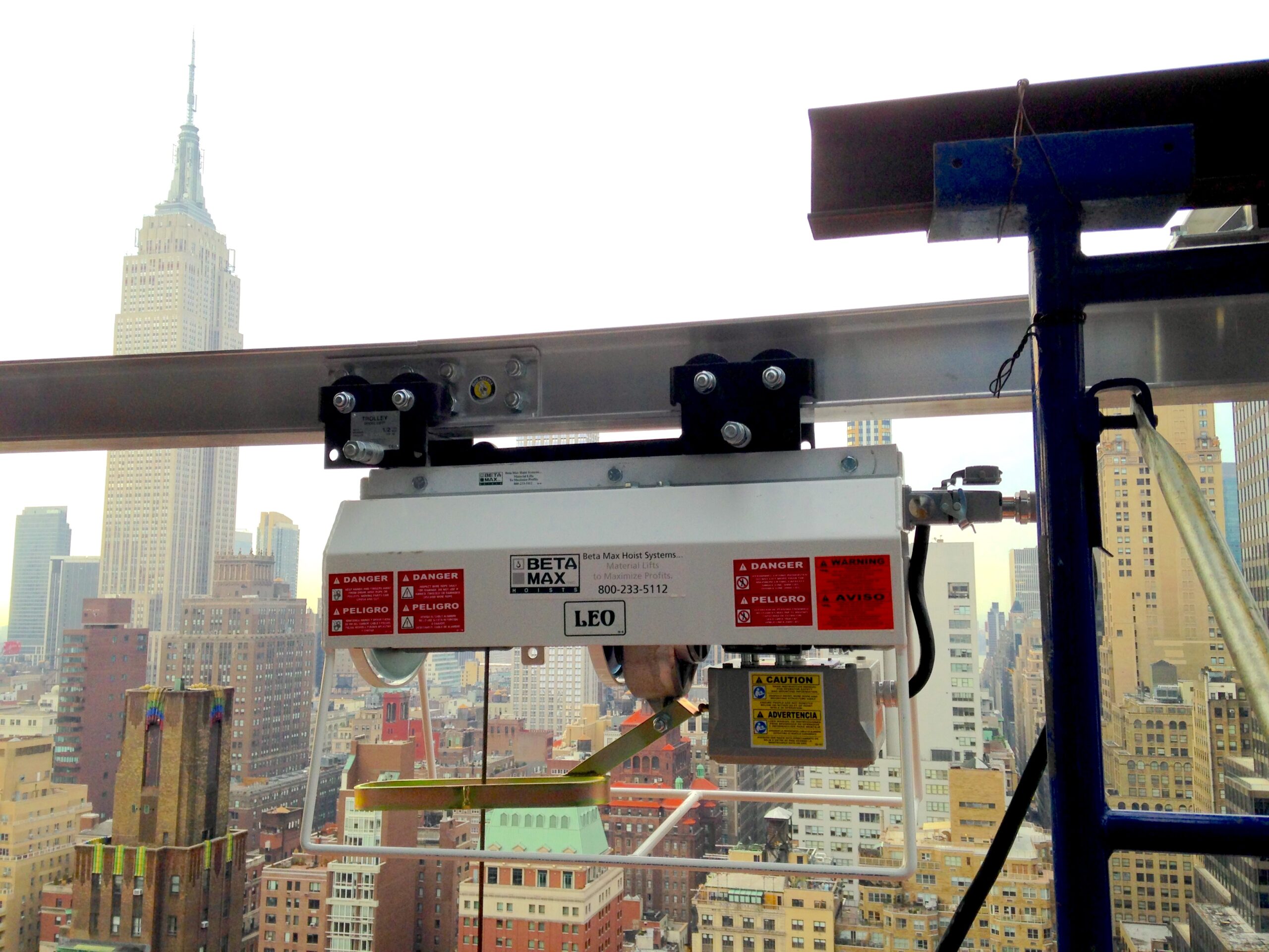 Jobsite photo of the Beta Max Leo Hoist attached to a track system, with the Empire State Building in the background.