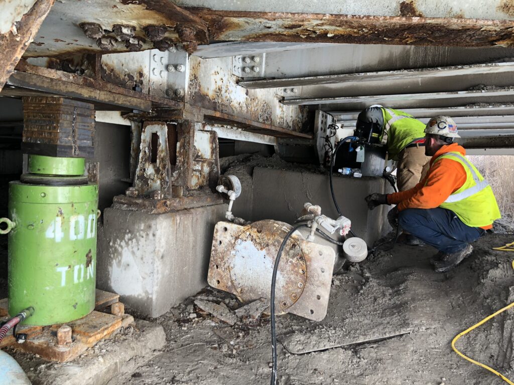 A jobsite photo of a hydraulic lifting system from LGH jacking up a bridge, with workers using the hydrualic pump.