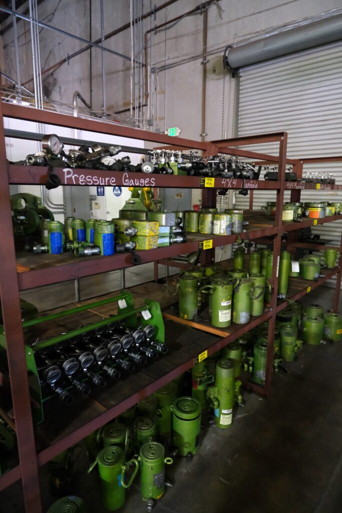 Photo of a rack shelf in the LGH rental center, stocked with hydraulic accessories like manifolds and gauges.