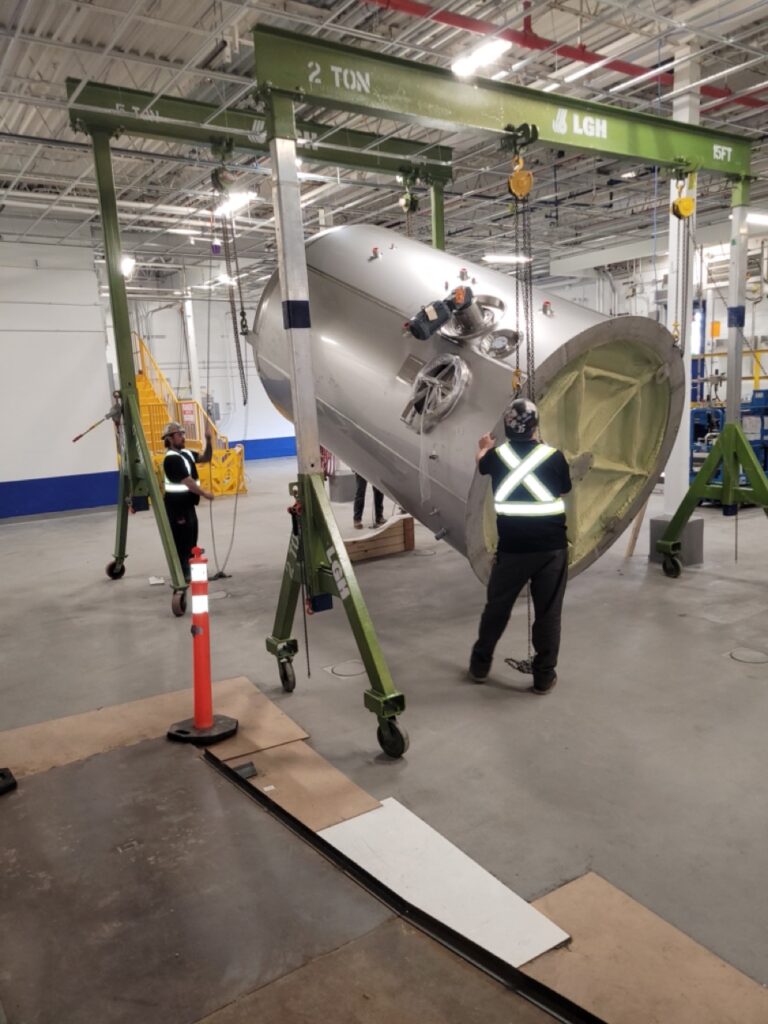 Two gantry crane rentals from LGH lifting a chocolate mixer in a factory.