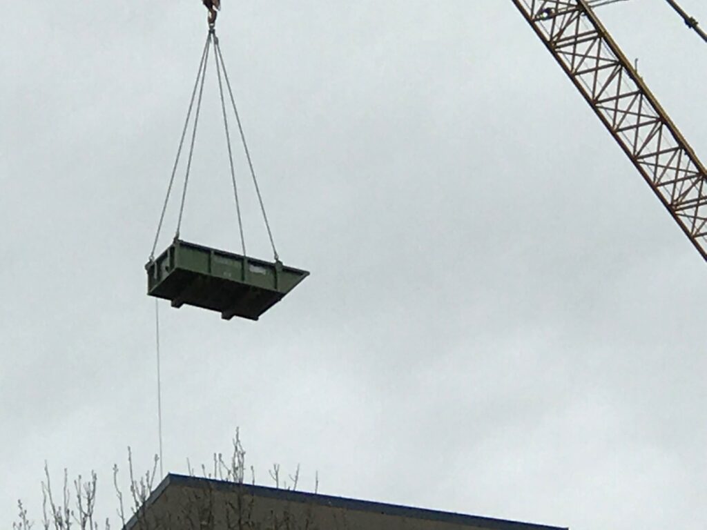 A photo of a crane skip pan hanging from a crane.
