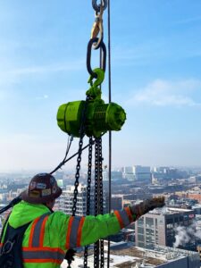 construction worker wearing safety vest and hard hat operating hand chain hoist on jobsite